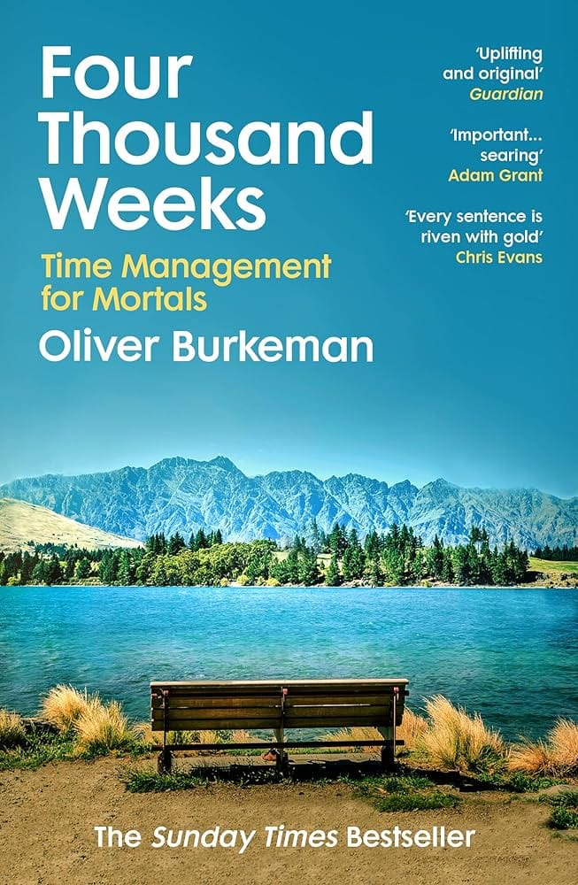 The cover for the book Four Thousand Weeks: a picture of an empty bench on shore of a lake with mountains in the distance; some blurbs on the cover.